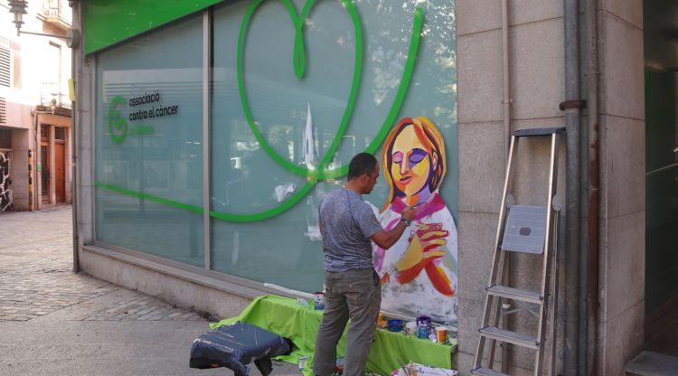 L'artista Pau Morales pinta un mural a la façana de l'Associació Contra el Càncer de Girona dins de la campanya 'Ens ho prenem a pit'. ACN