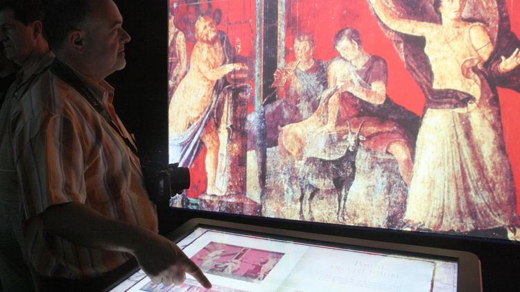 Un visitant toca el llibre virtual amb frescos trobats a les ciutats vesuvianes © ACN