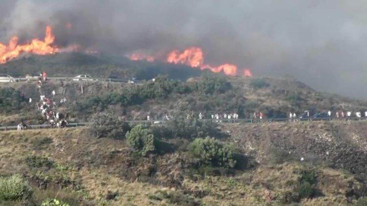 Diverses persones baixen per un barranc fugint del foc que arriba a la N-260, a Portbou