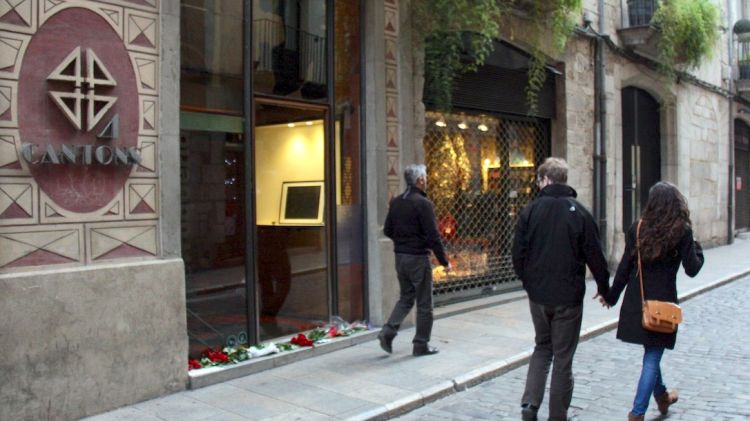 Diversos ciutadans miren l'entrada de l'establiment on hi ha roses i targetes en record a una de les víctimes © ACN